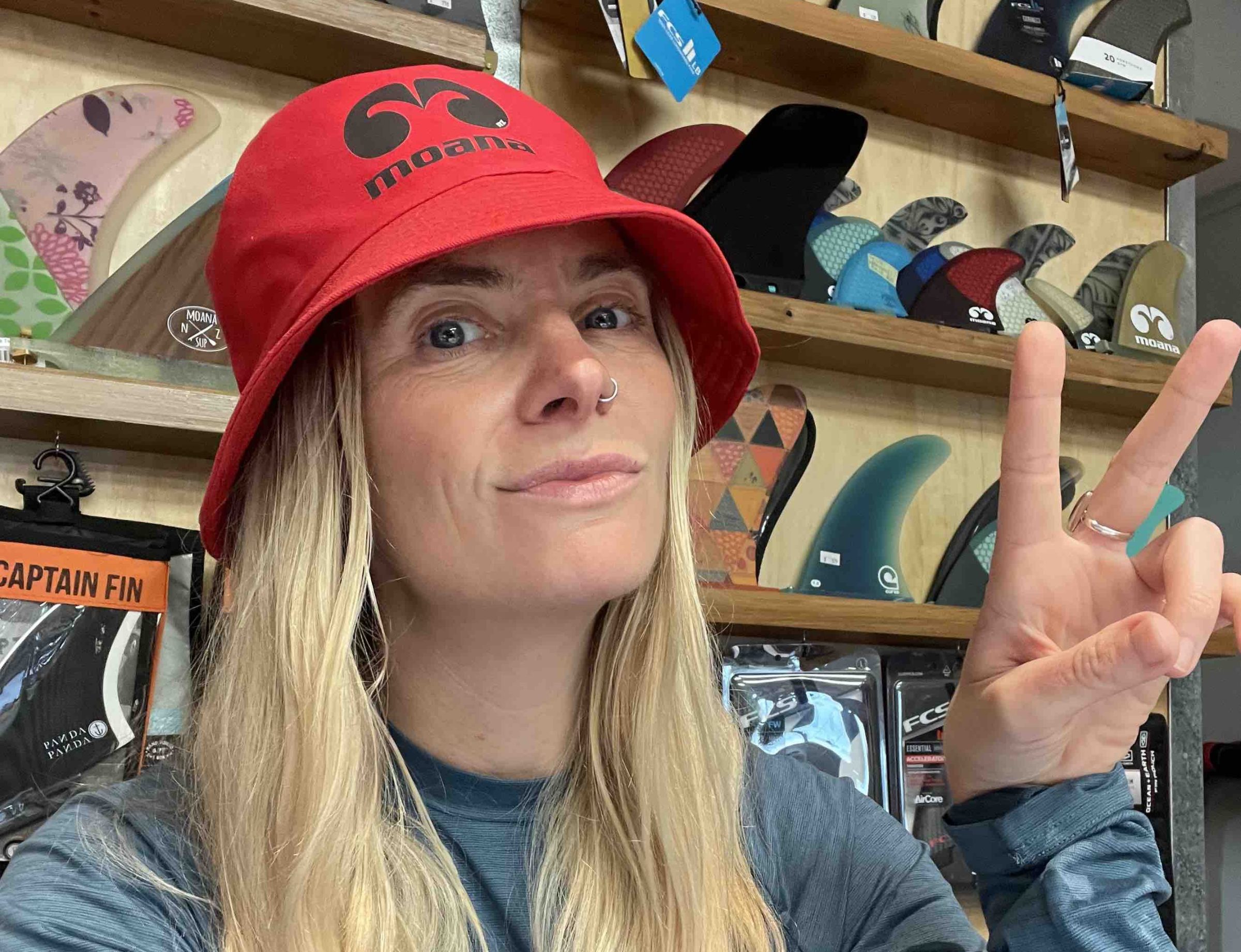 Person in red hat making peace sign in front of surfboard fins display.